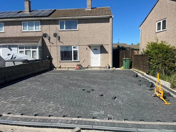 Dark grey block paving driveway part way through being laid, with a block cutter and channel drain