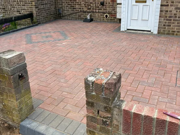 Red block paving front garden with a grey diamond feature, between brick gate pillars